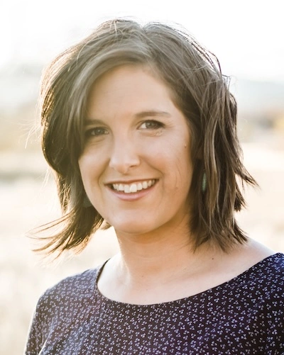 Headshot of Sarah R. Eisenbud, MA, NCC, Integrative Narrative Therapist. Sarah wears her hair in a chin-length bob and a purple scoop-neck tunic. She looks directly at the camera, smiling.